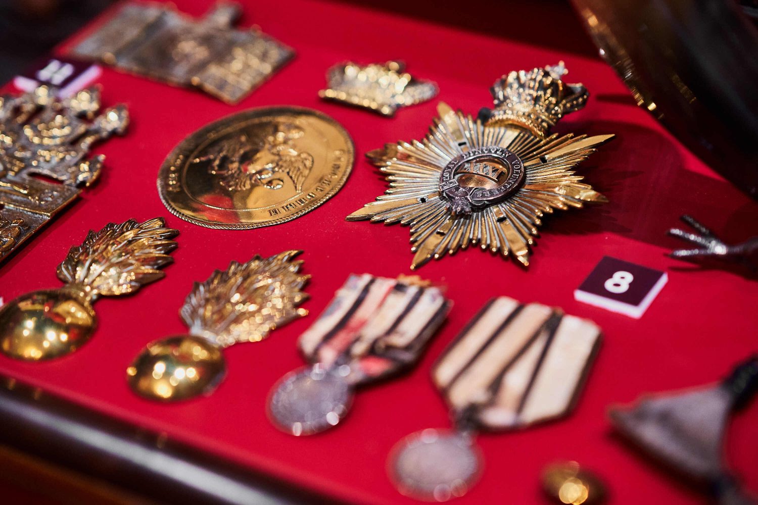 A red display case with 8 medals inside of different shapes and sizes