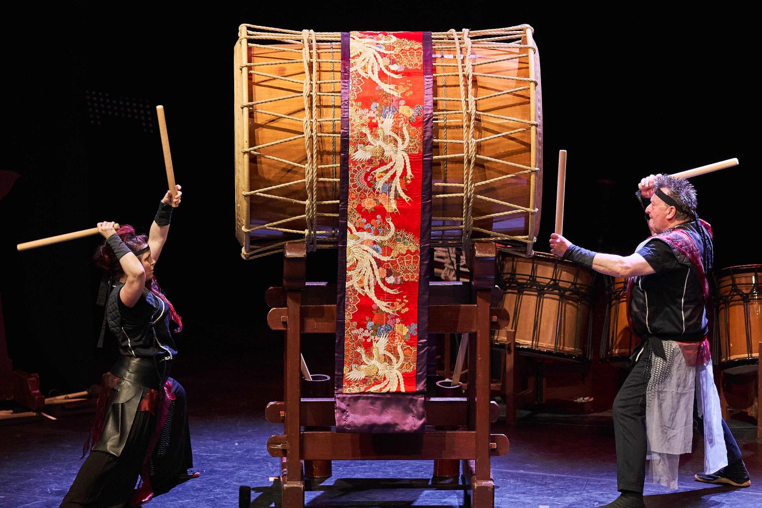 two men, on stage, banging on a giant drum