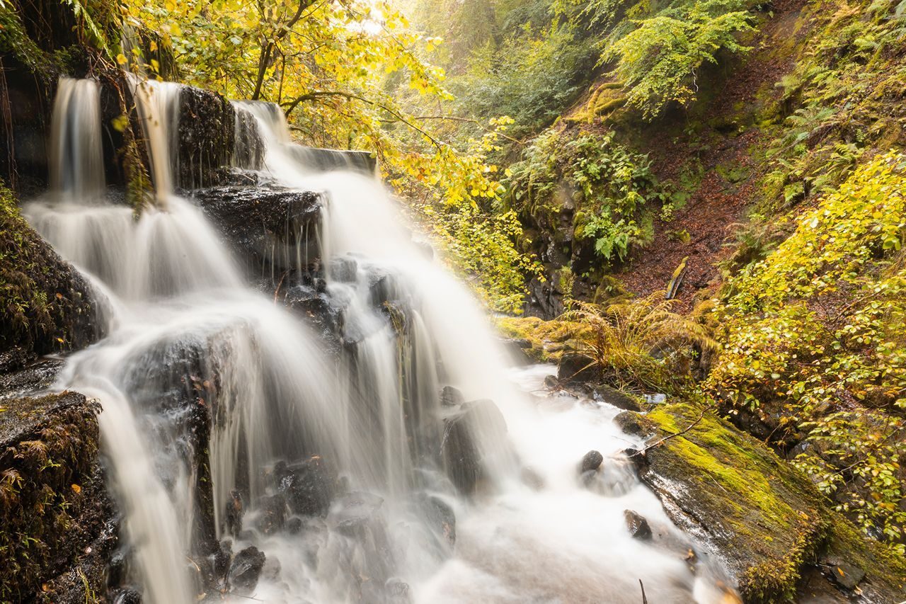 A waterfall over rugged rocks set amongst green trees and hillsides