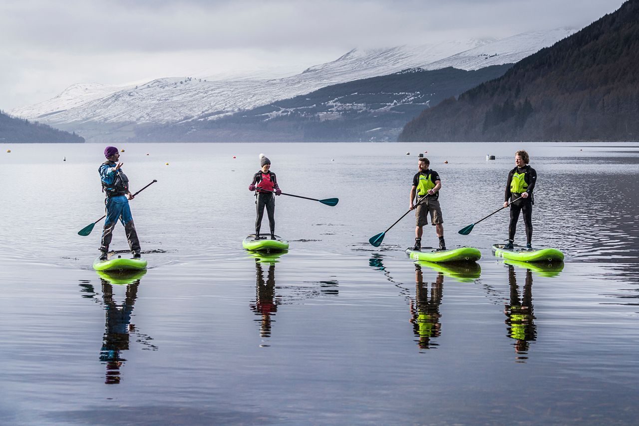 four people paddleboarding on a Scottish Loch with mountains behind and grey overcast skies