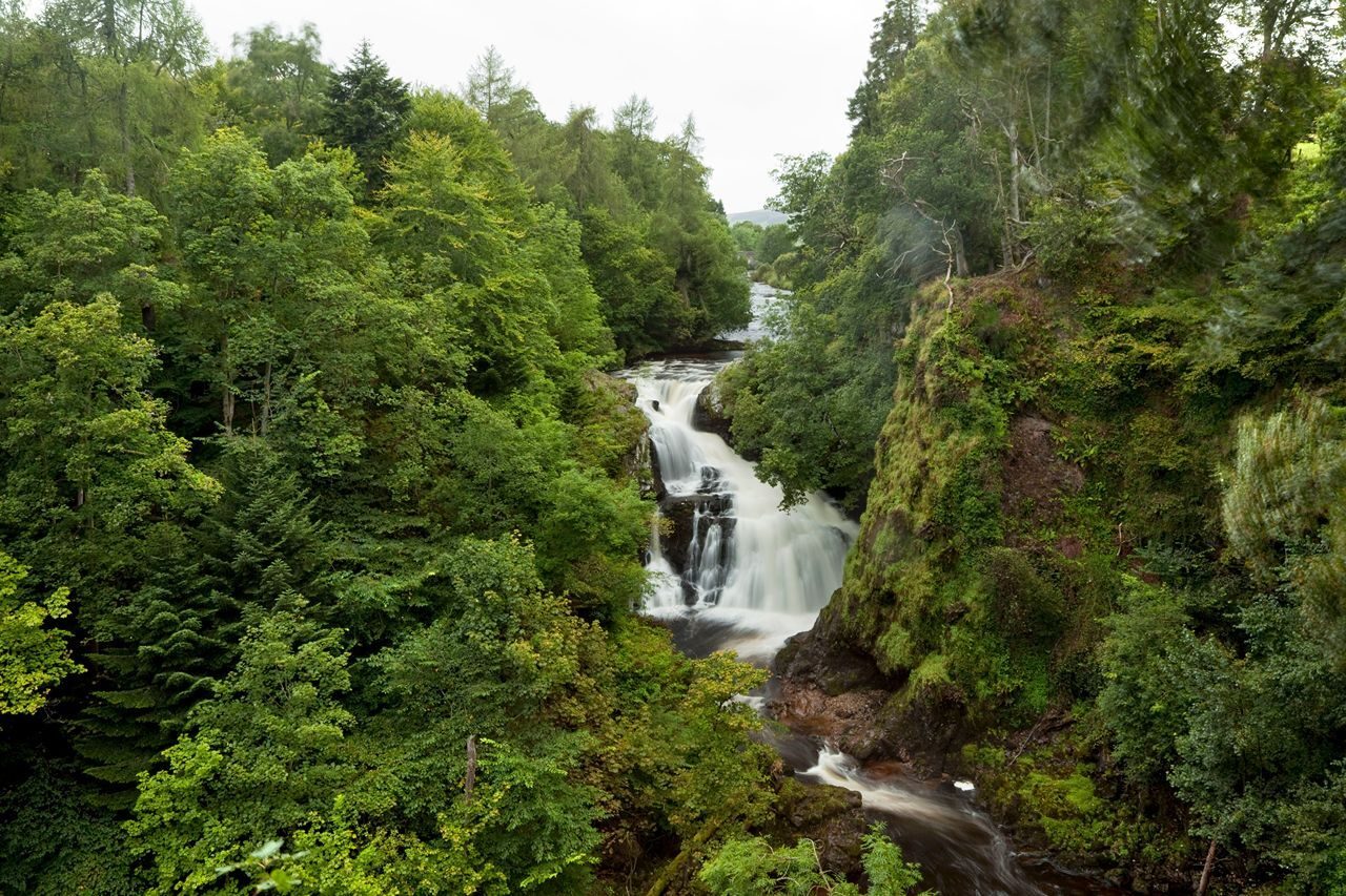 A waterfall set amongst lush green trees in Scotland