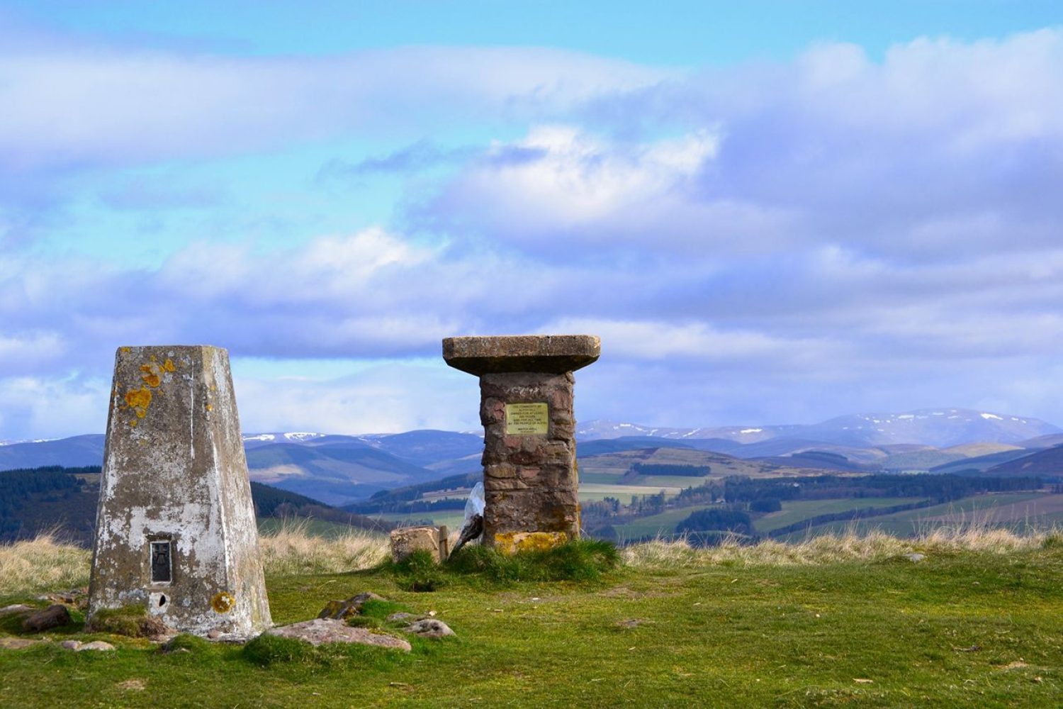 stone pillars on a hill top overlooking Scottish countryside below bright blue sky
