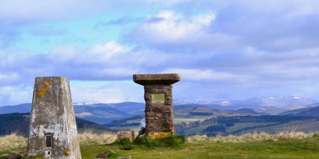 stone pillars on a hill top overlooking Scottish countryside below bright blue sky