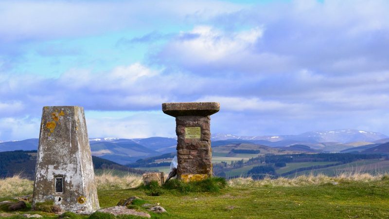 stone pillars on a hill top overlooking Scottish countryside below bright blue sky
