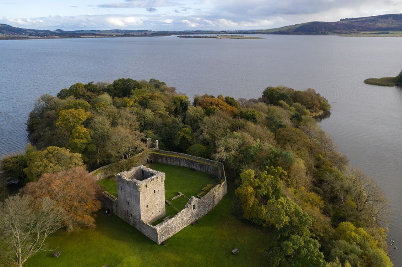 castle in walled perimeter on an island on a loch surrounded by green trees