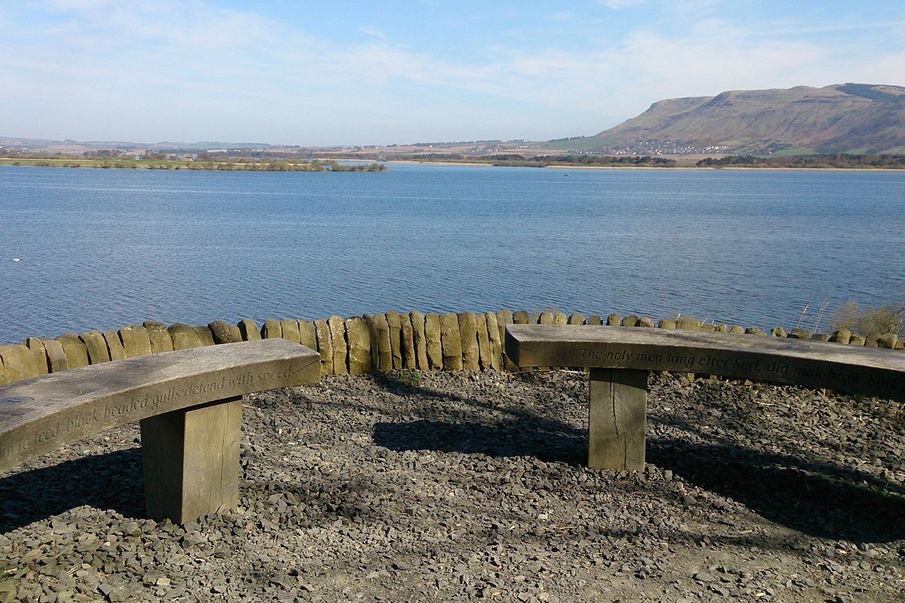 stone chairs overlooking wide expanse of water towards blue skies and hillsides