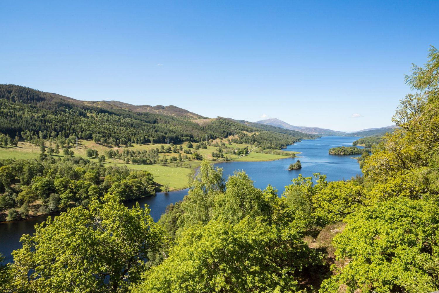 Blue skies on a summer day stretching across a winding blue river surrounded by lush green trees and Scottish hills