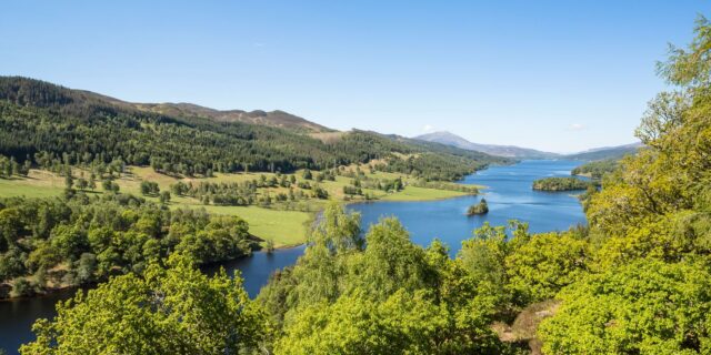 Blue skies on a summer day stretching across a winding blue river surrounded by lush green trees and Scottish hills