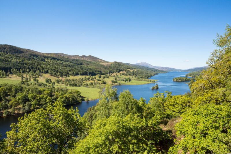 Blue skies on a summer day stretching across a winding blue river surrounded by lush green trees and Scottish hills