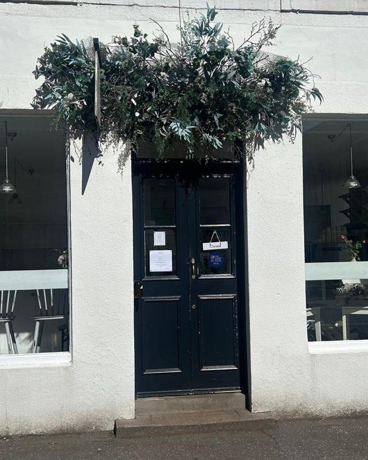White building with black door and two windows with dried flower arrangement above door,  Bakery in Dunkeld.