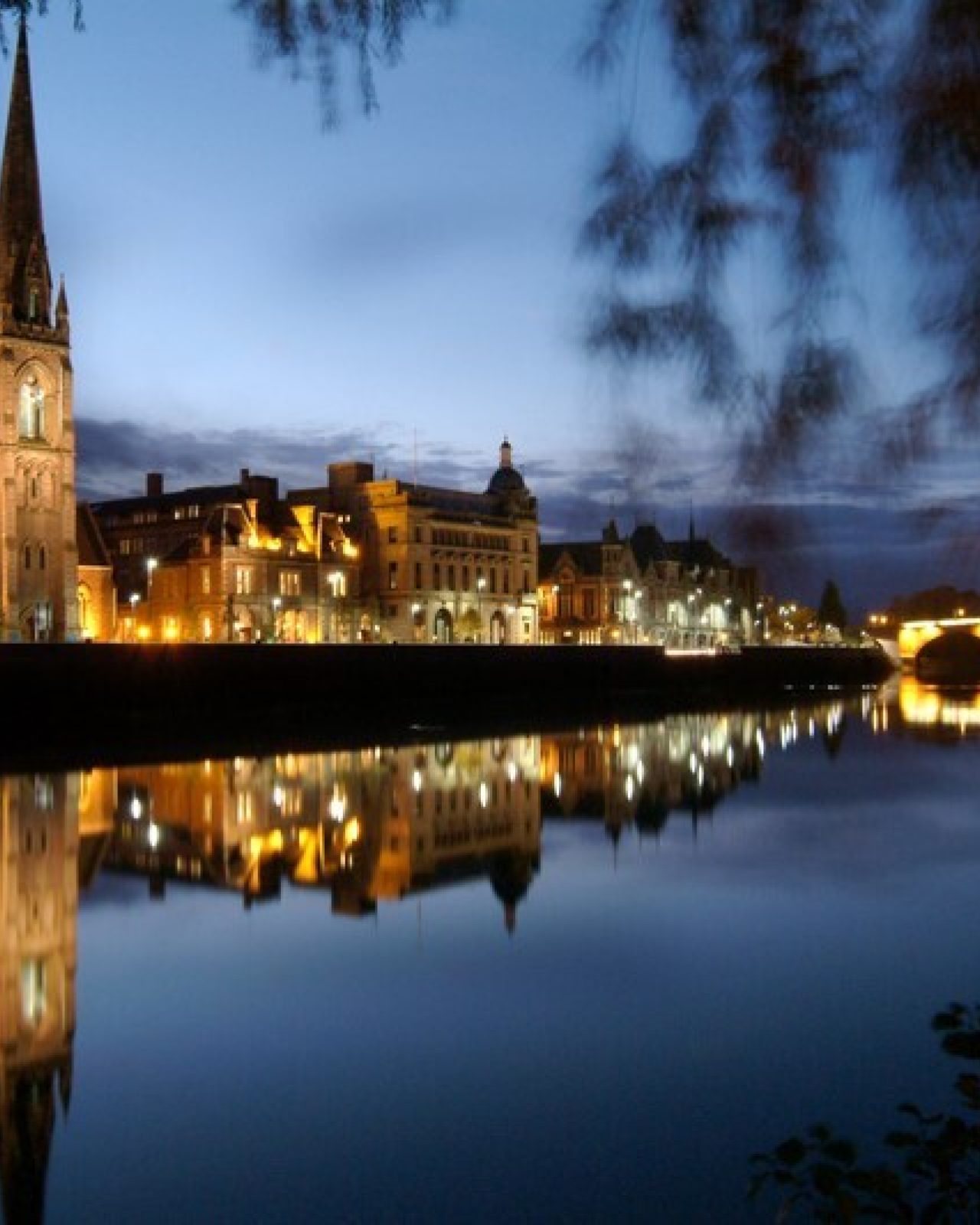 A large lit up church and stone bridge can be seen across the River Tay