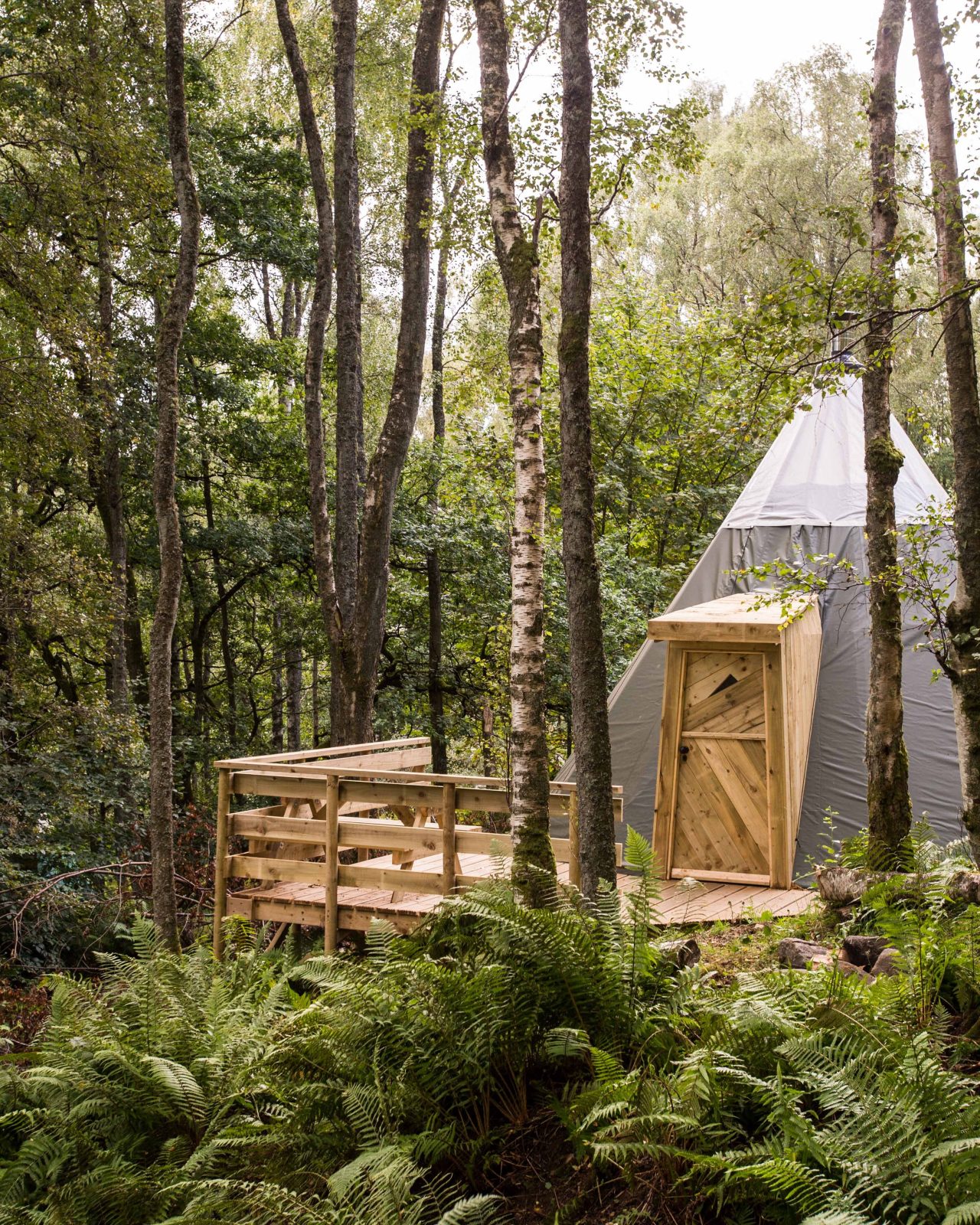 A grey tent sits on a wooden porch in a forest
