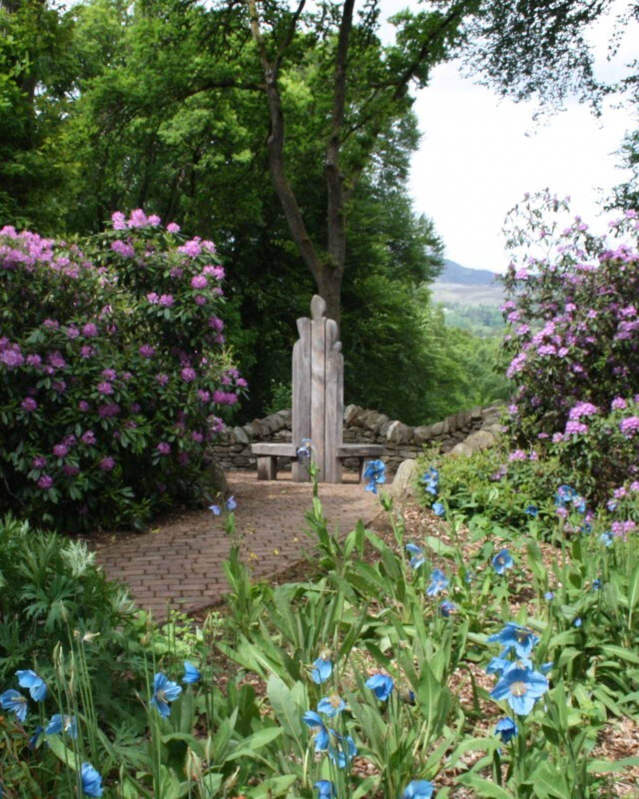 A lush garden full of bushes and flowers with a small sculpture in the middle