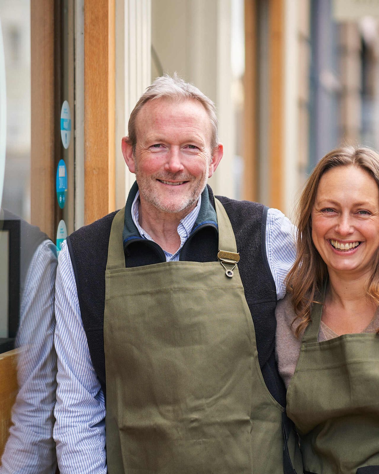 A man wearing an apron rests his hand on the shoulder of a woman wearing an apron