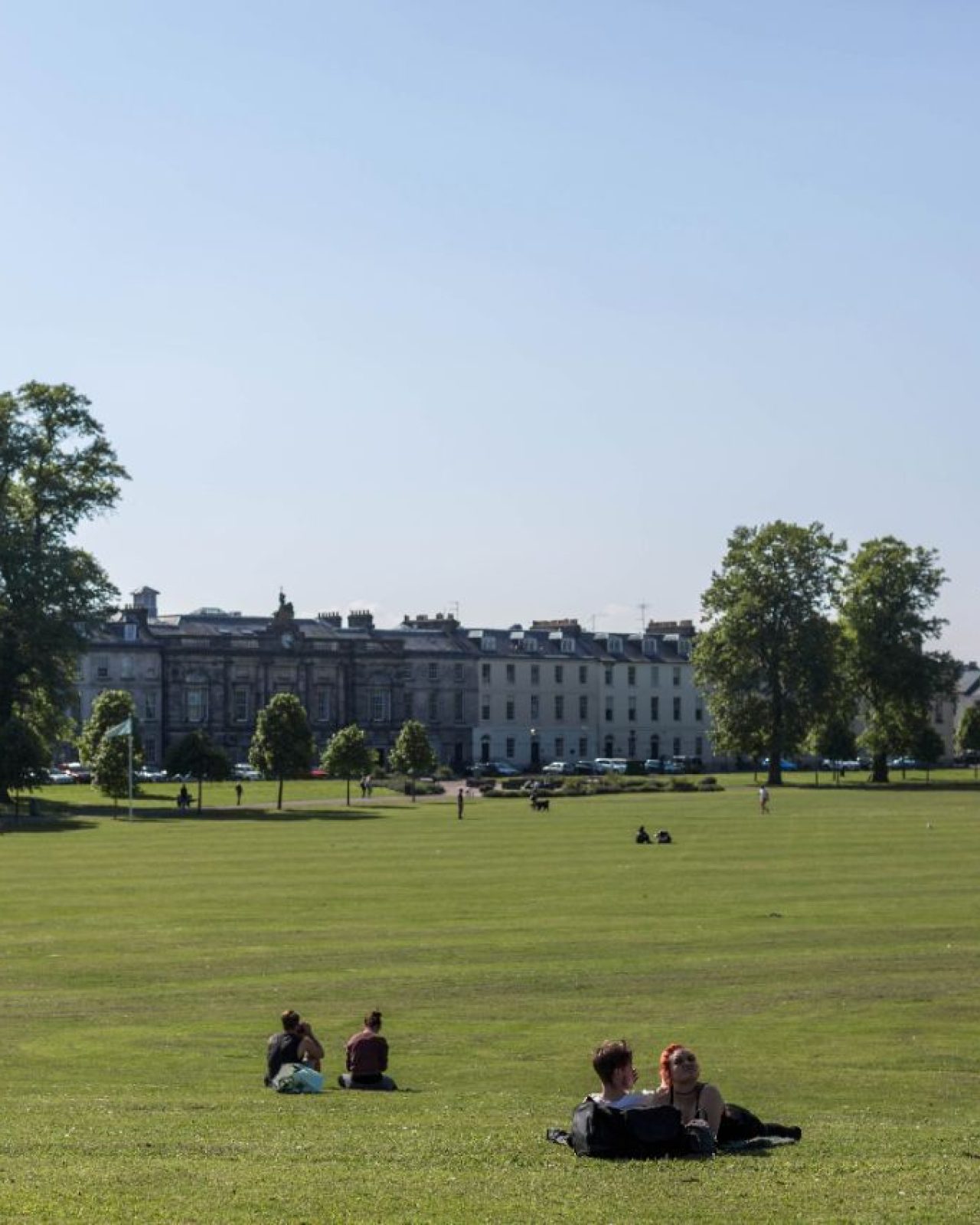 a wide green parklands with people sunbathing and trees lining the walk