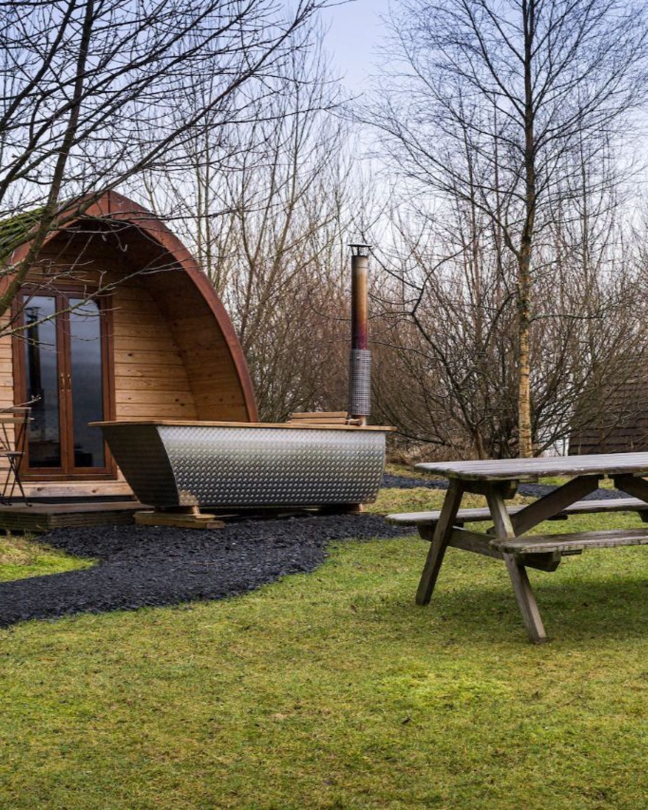 A wooden wigwam sits on a green lawn next to outside furniture
