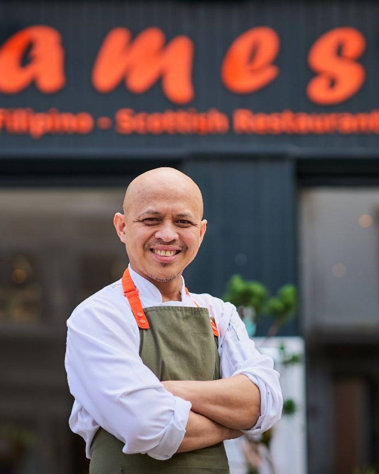 a chef standing outside a black budling with orange signage