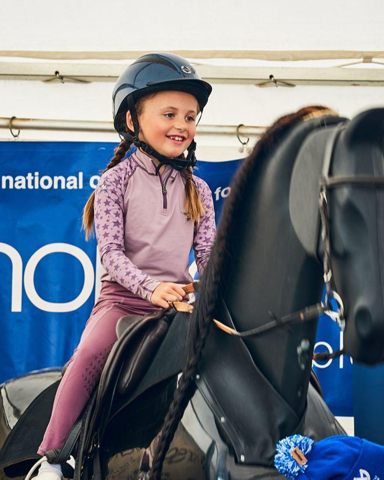 a young girl in lilac jumper on a horse simulator