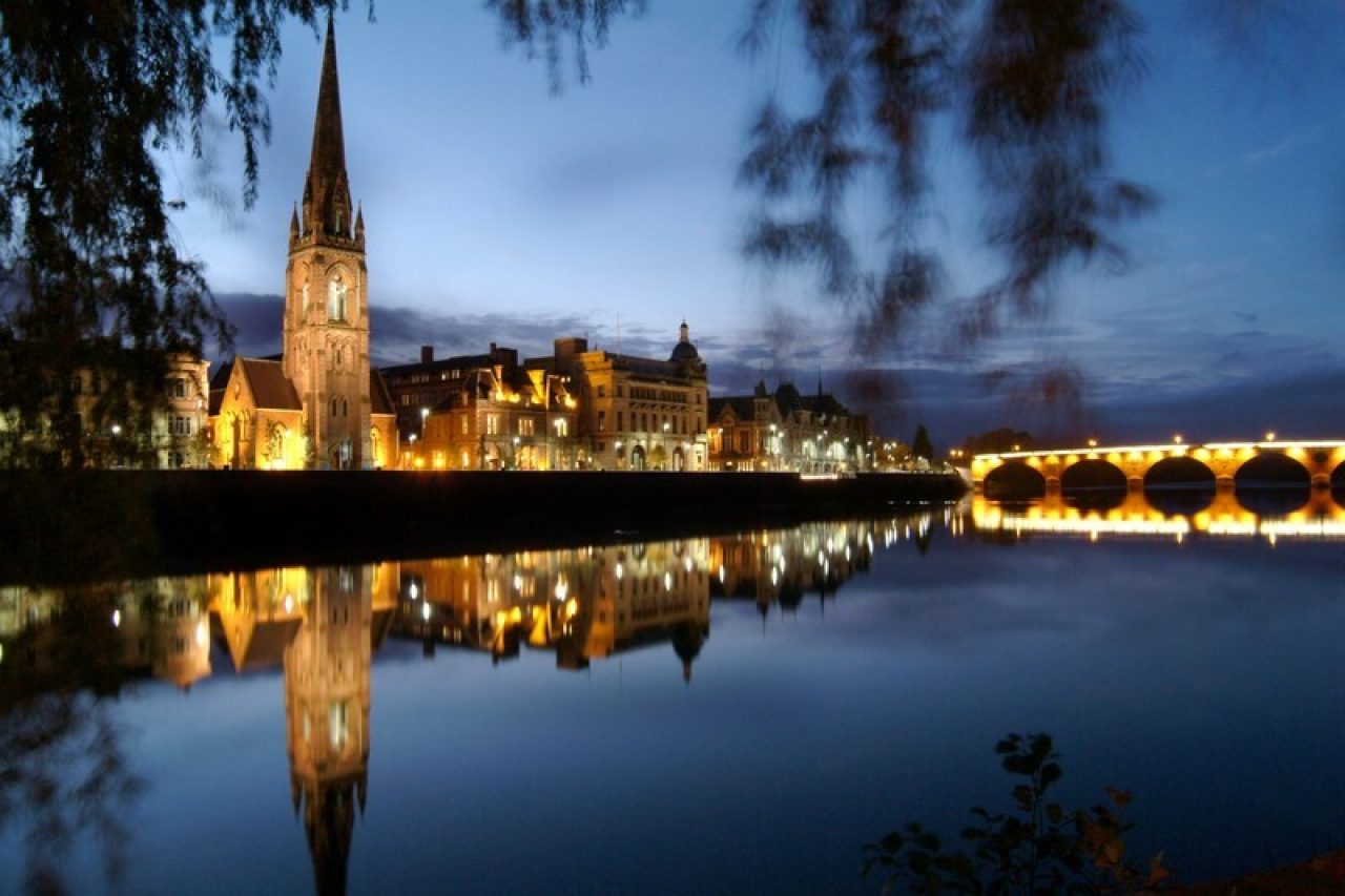 A large lit up church and stone bridge can be seen across the River Tay