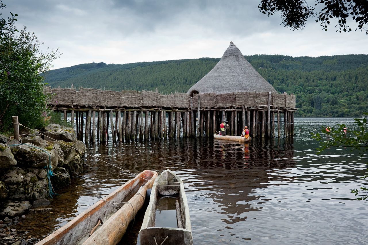 Wooden boats on Scottish loch in front of ancient crannog structure