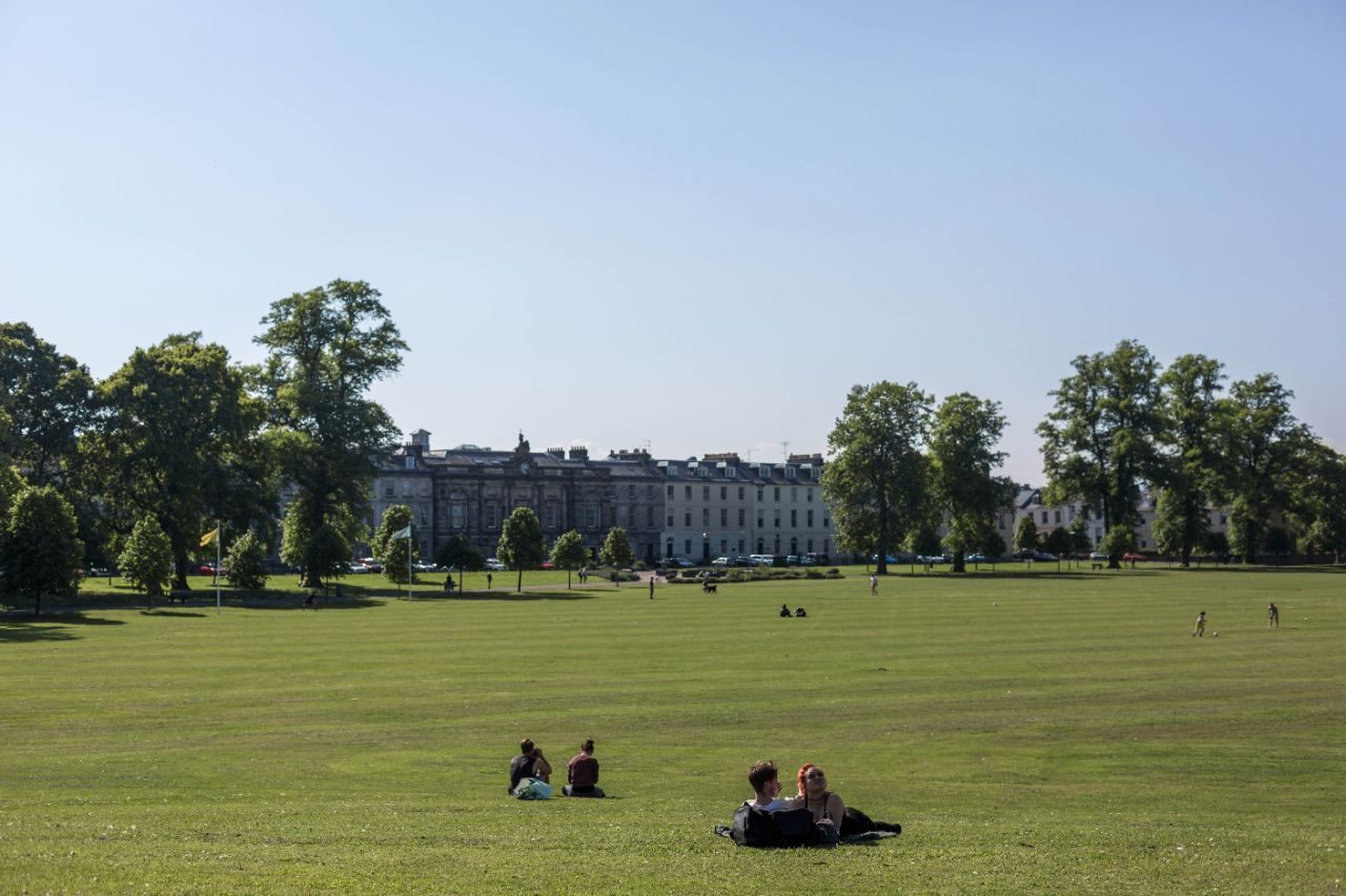 a wide green parklands with people sunbathing and trees lining the walk