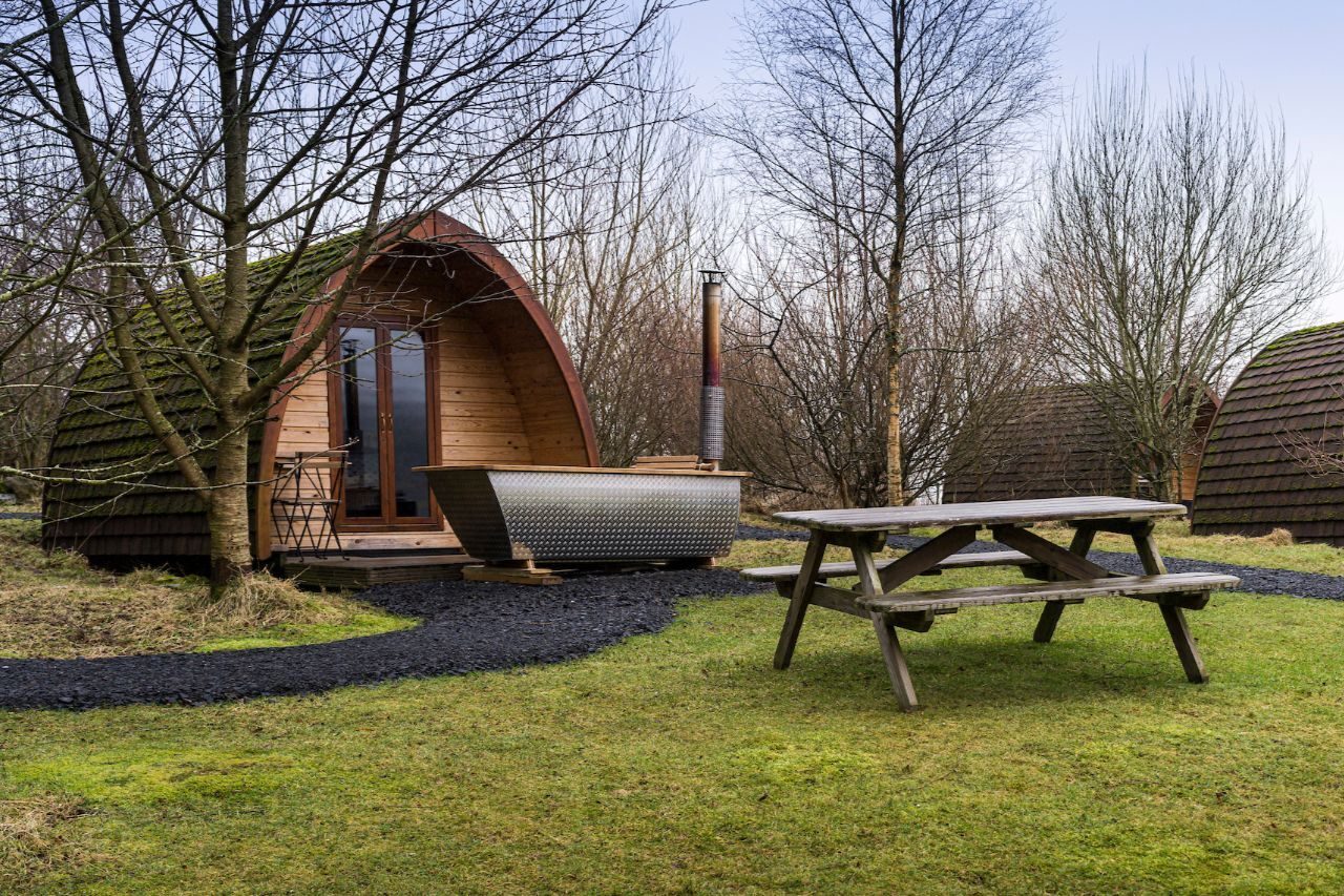 A wooden wigwam sits on a green lawn next to outside furniture