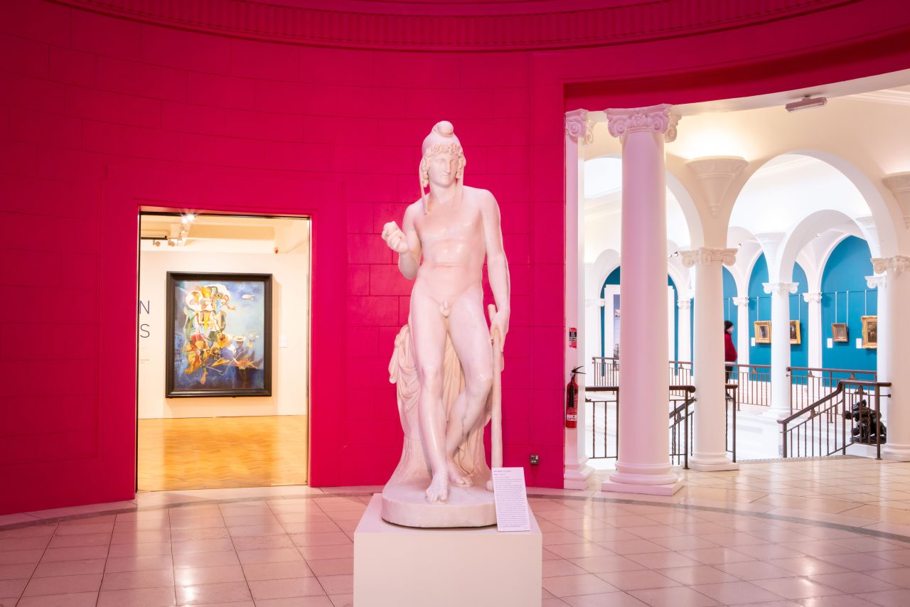A white statue of a man stands in the middle of a circular pink hall