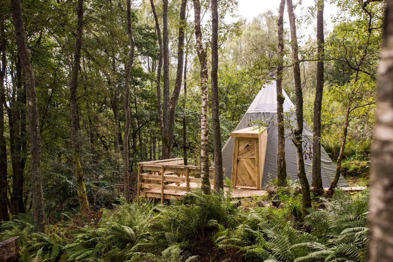 A grey tent sits on a wooden porch in a forest