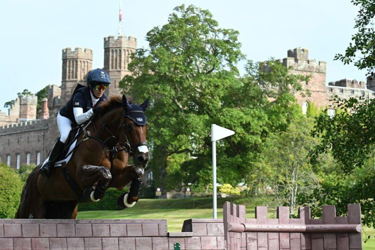 Woman on horse jumping over fence in front of Scone Palace at the International Horse Trials