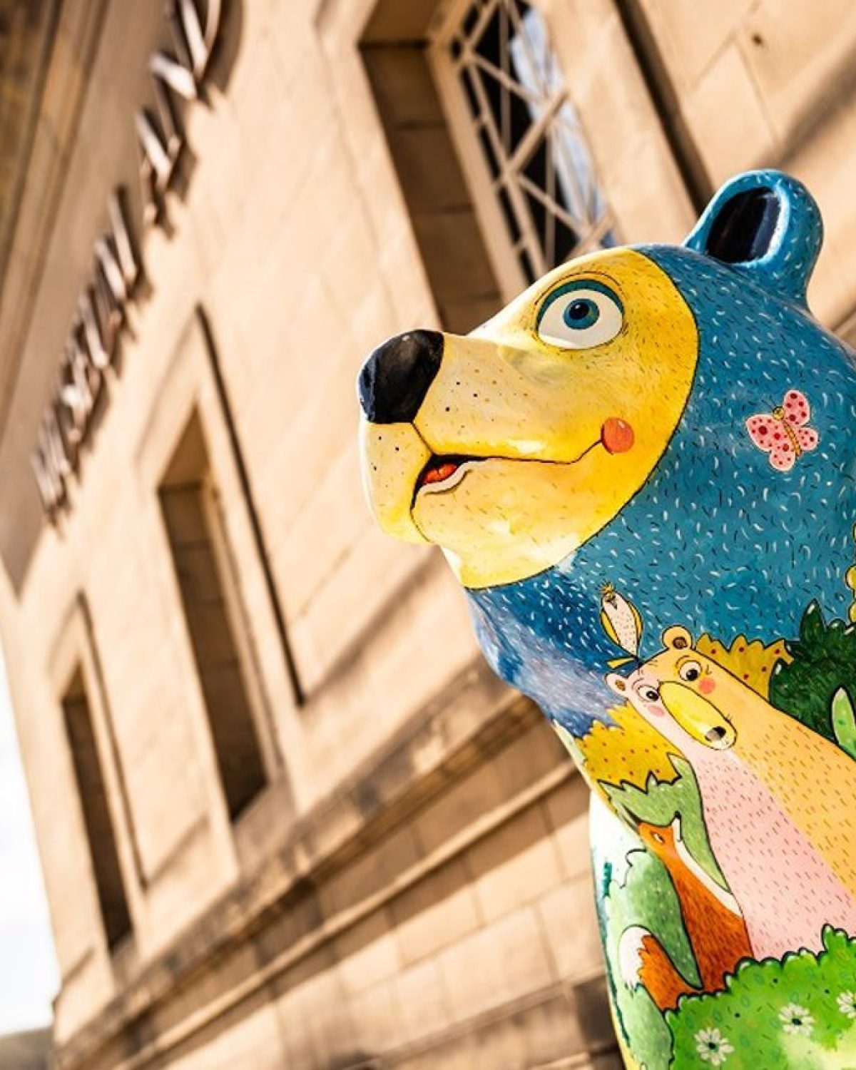 A colourful bear with different woodland animals enjoying a meadow