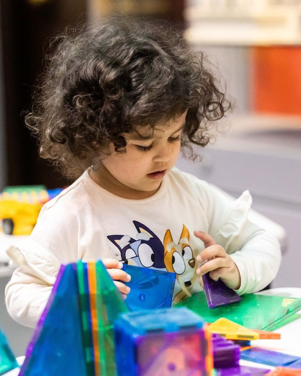Curly haired small child playing with colourful small shapes.