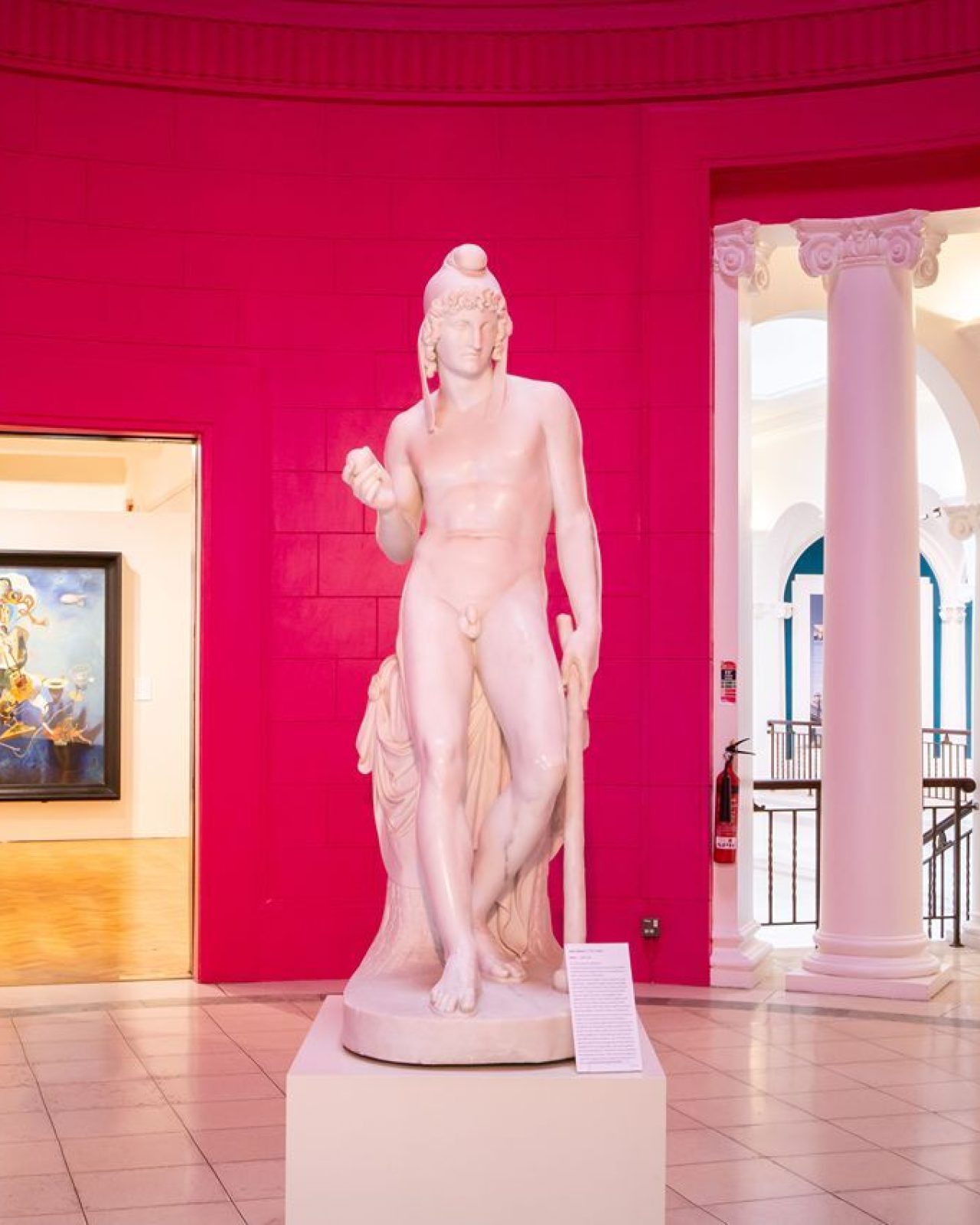 White statue standing in a bright pink room, leading to a white columned hallway in Perth Art Gallery