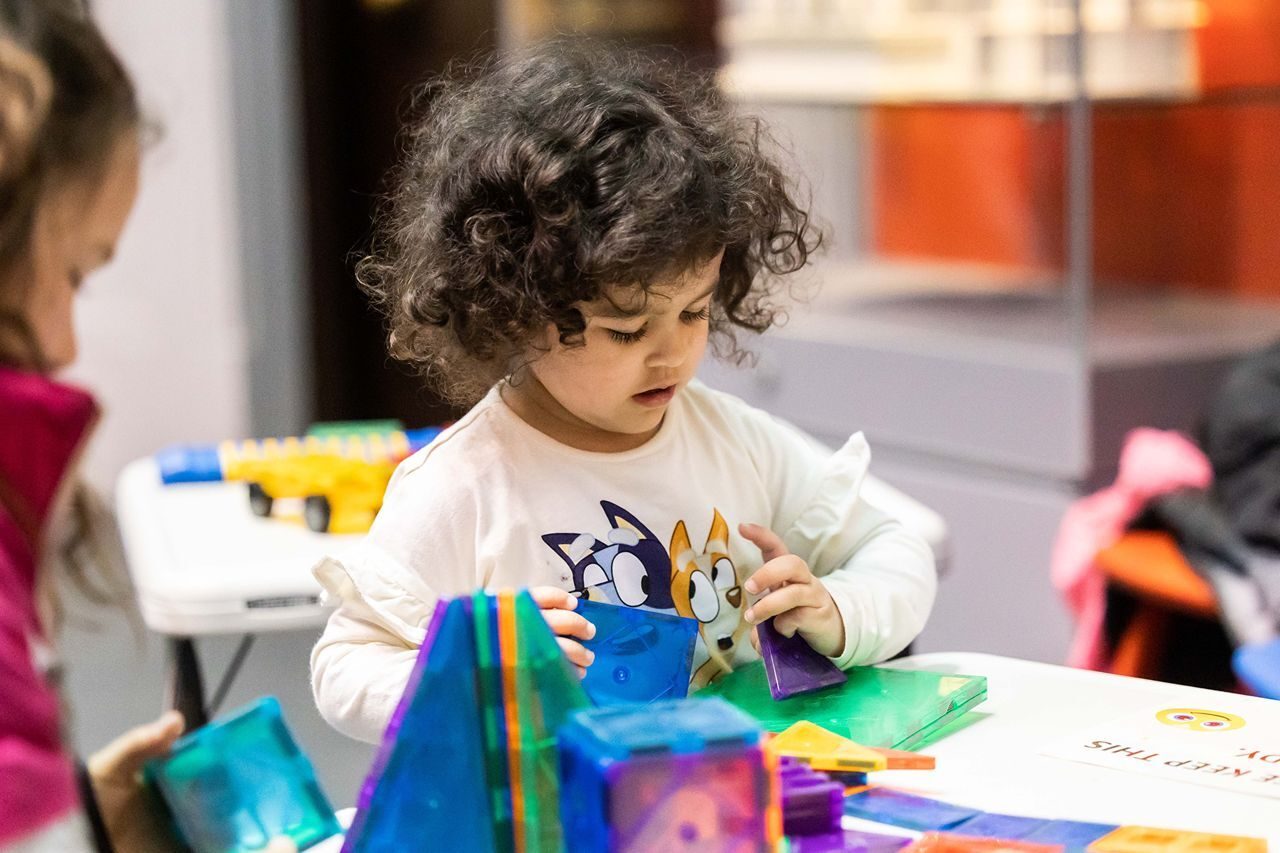 Curly haired small child playing with colourful small shapes.