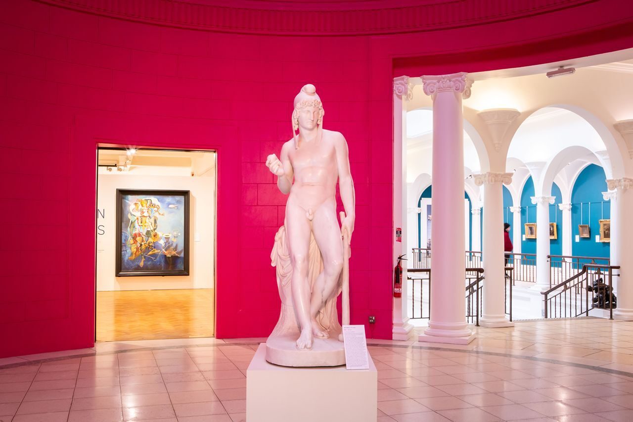 White statue standing in a bright pink room, leading to a white columned hallway in Perth Art Gallery