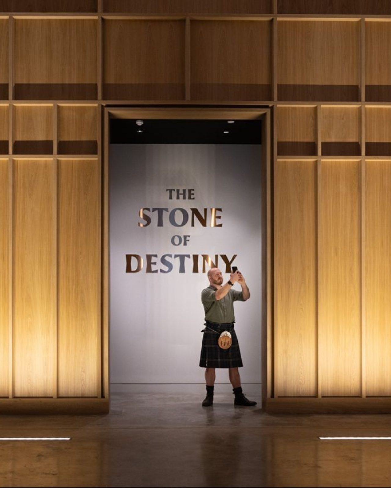 Man in kilt with phone standing in front of Stone of Destiny in Perth Museum