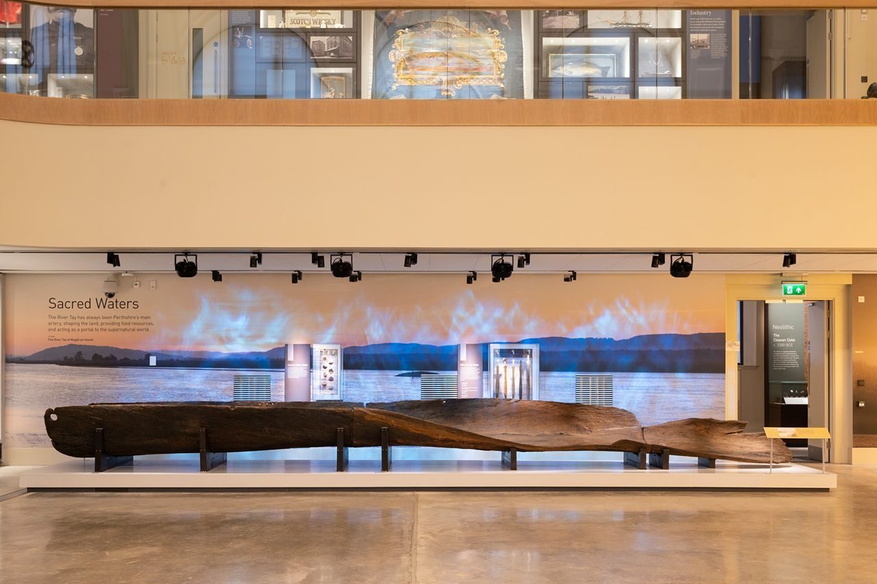 Large old wooden boat displayed in a bright modern museum.
