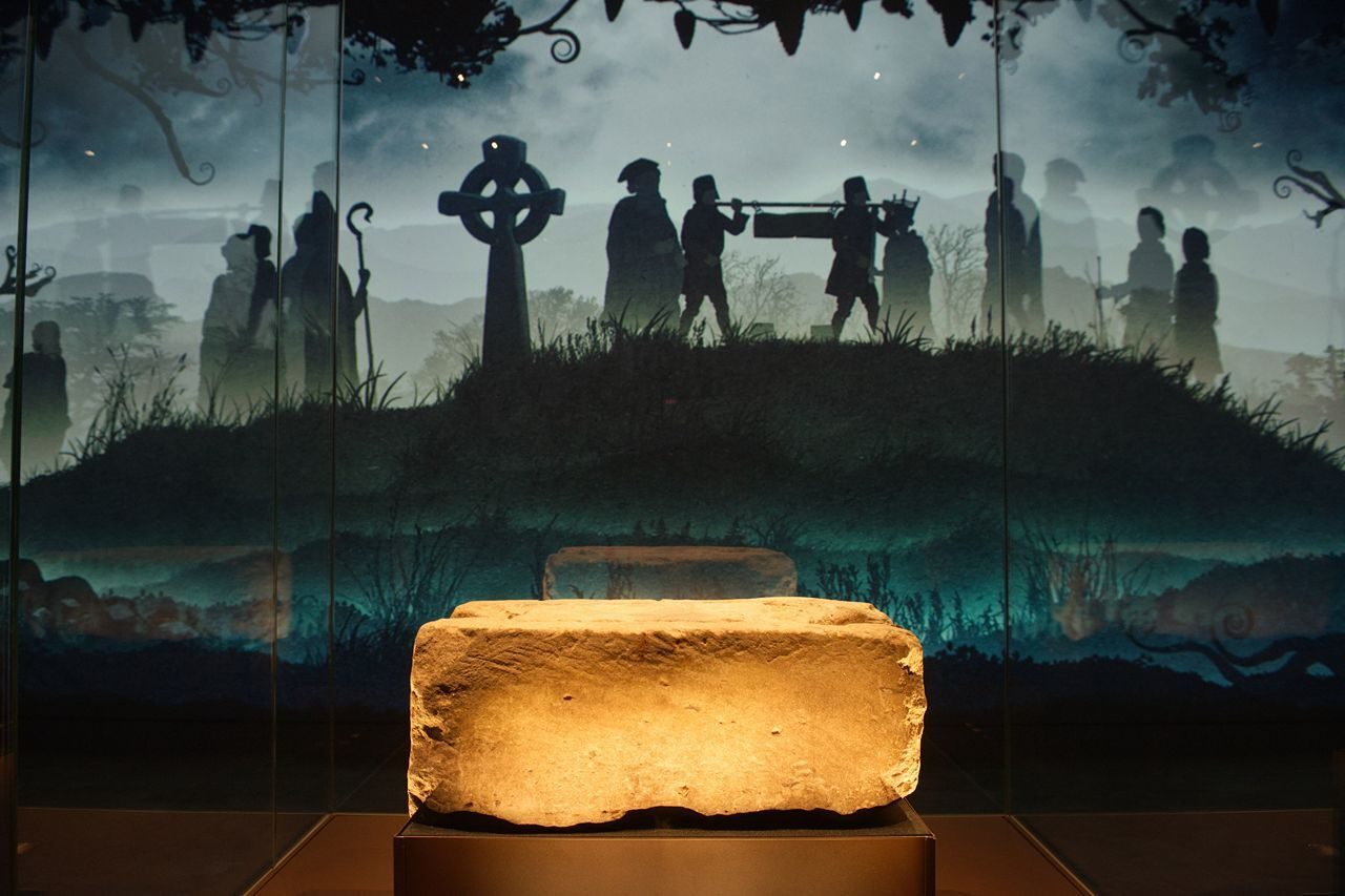 Large sandstone block in front of images of old crosses and people