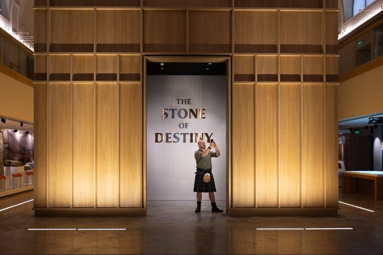 Man in kilt with phone standing in front of Stone of Destiny in Perth Museum