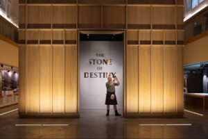 Man in kilt with phone standing in front of Stone of Destiny in Perth Museum