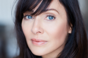 Dark haired woman, with large pale blue eyes.