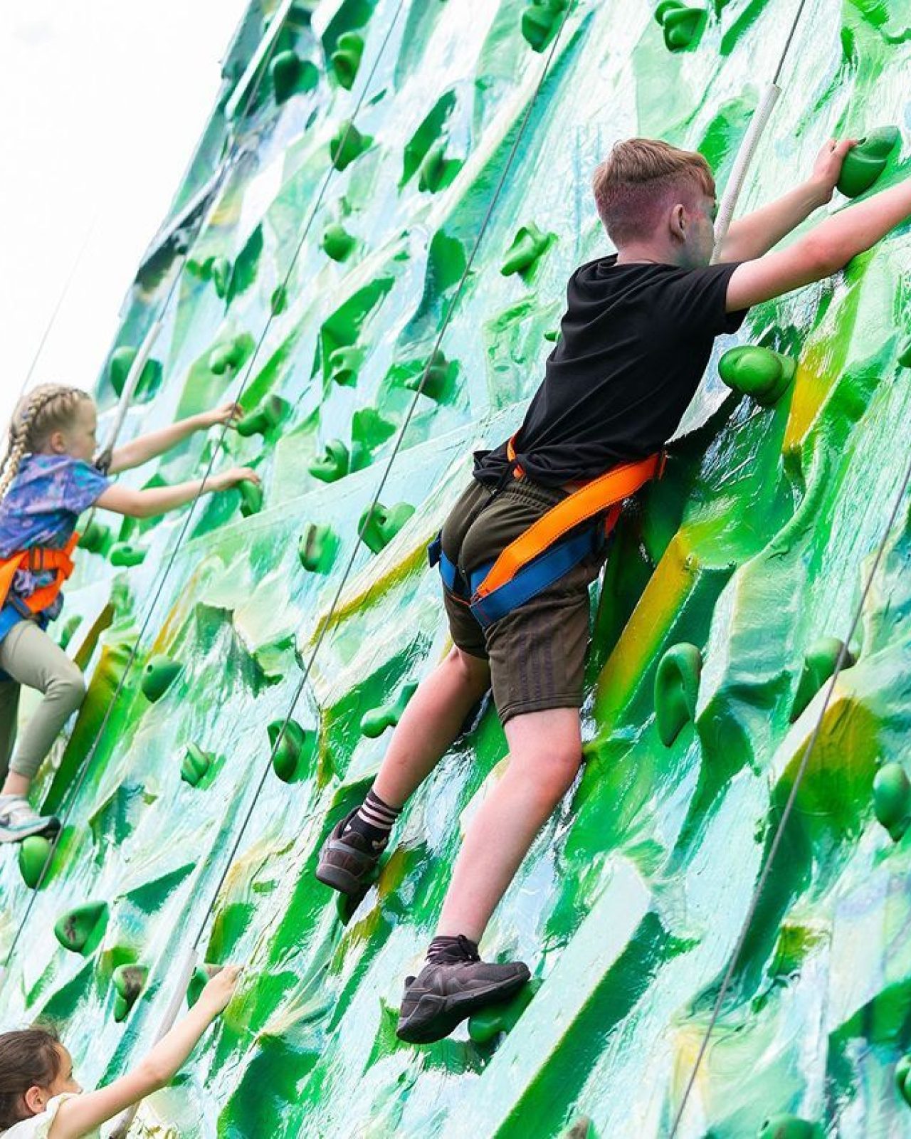 Two children wearing harnesses on a green climbing wall