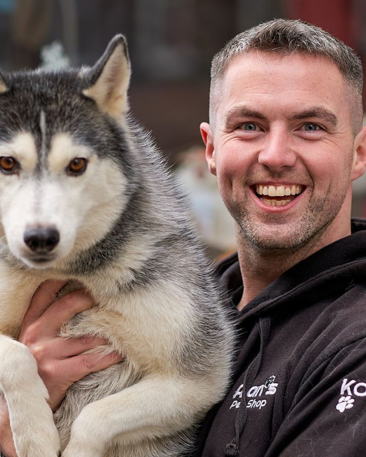 Smiling dark haired man holding a Siberian husky dog in his arms.
