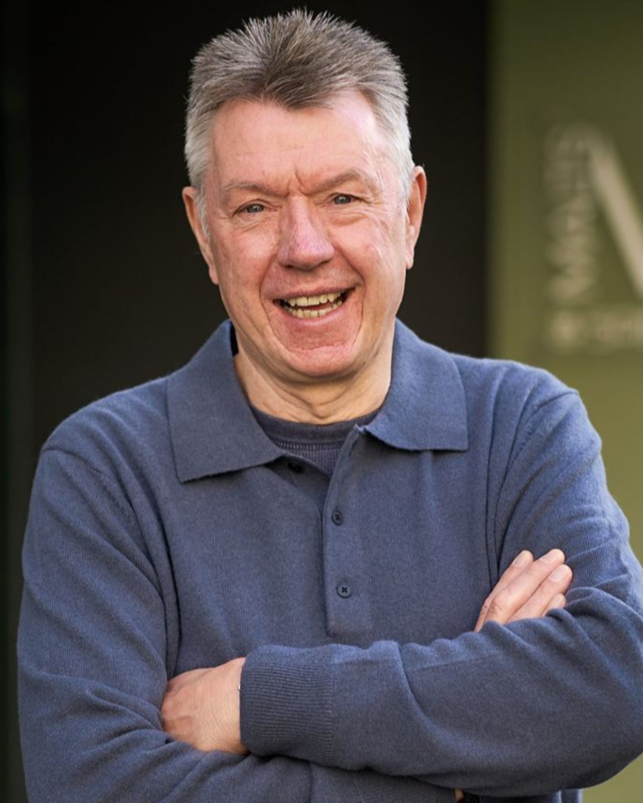 Smiling man wearing a dark blue jumper, with crossed arms stands in front of Malts & Spirts sign