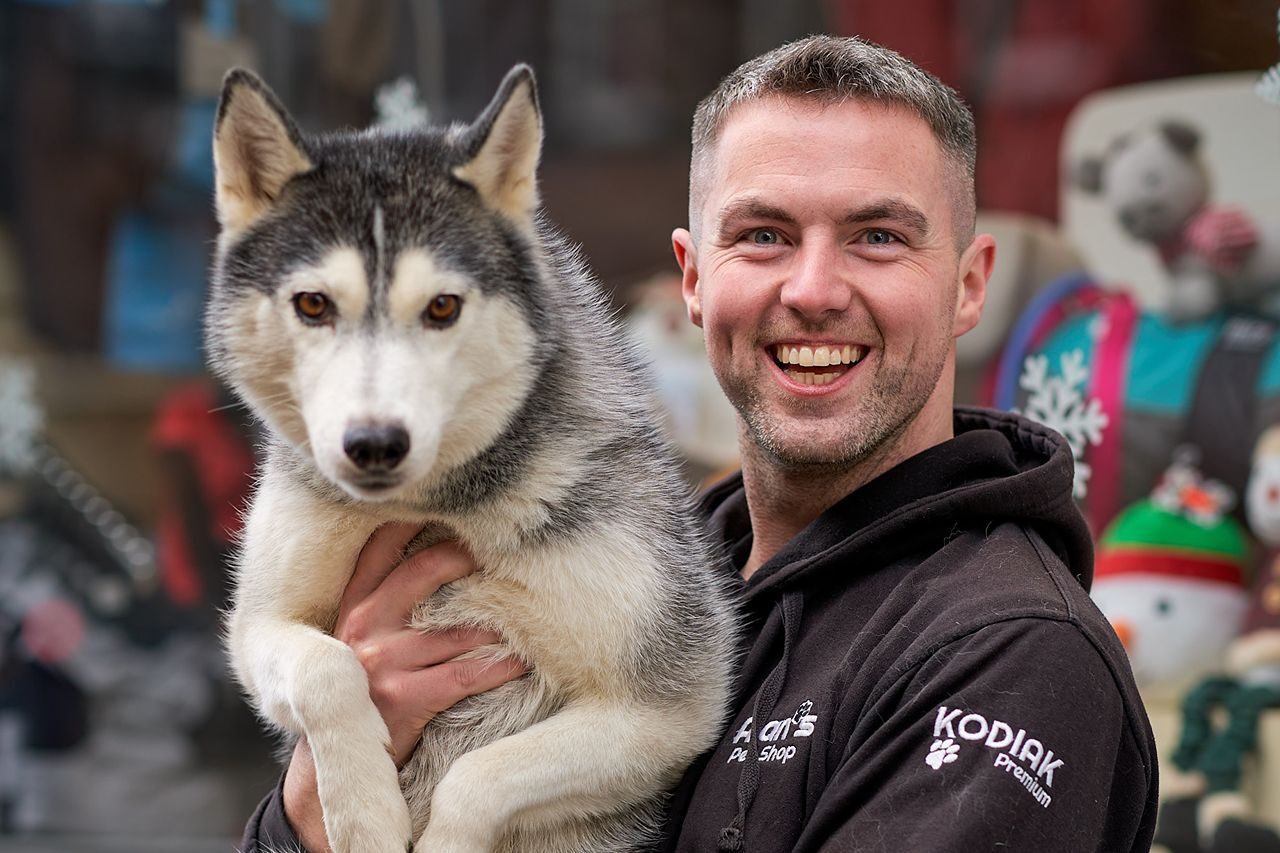Smiling dark haired man holding a Siberian husky dog in his arms.