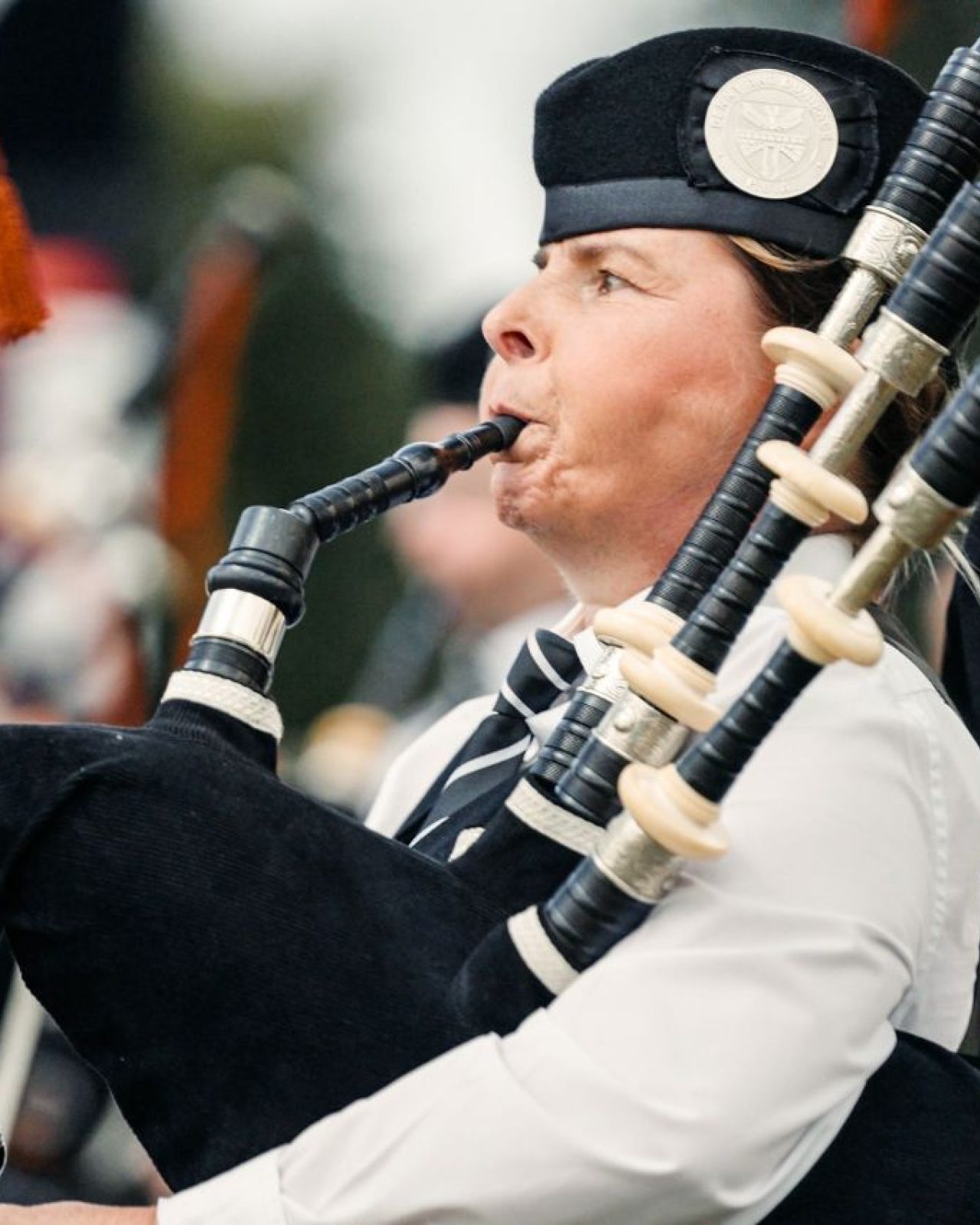 A woman in a white shirt playing black bagpipes with orange tassels.