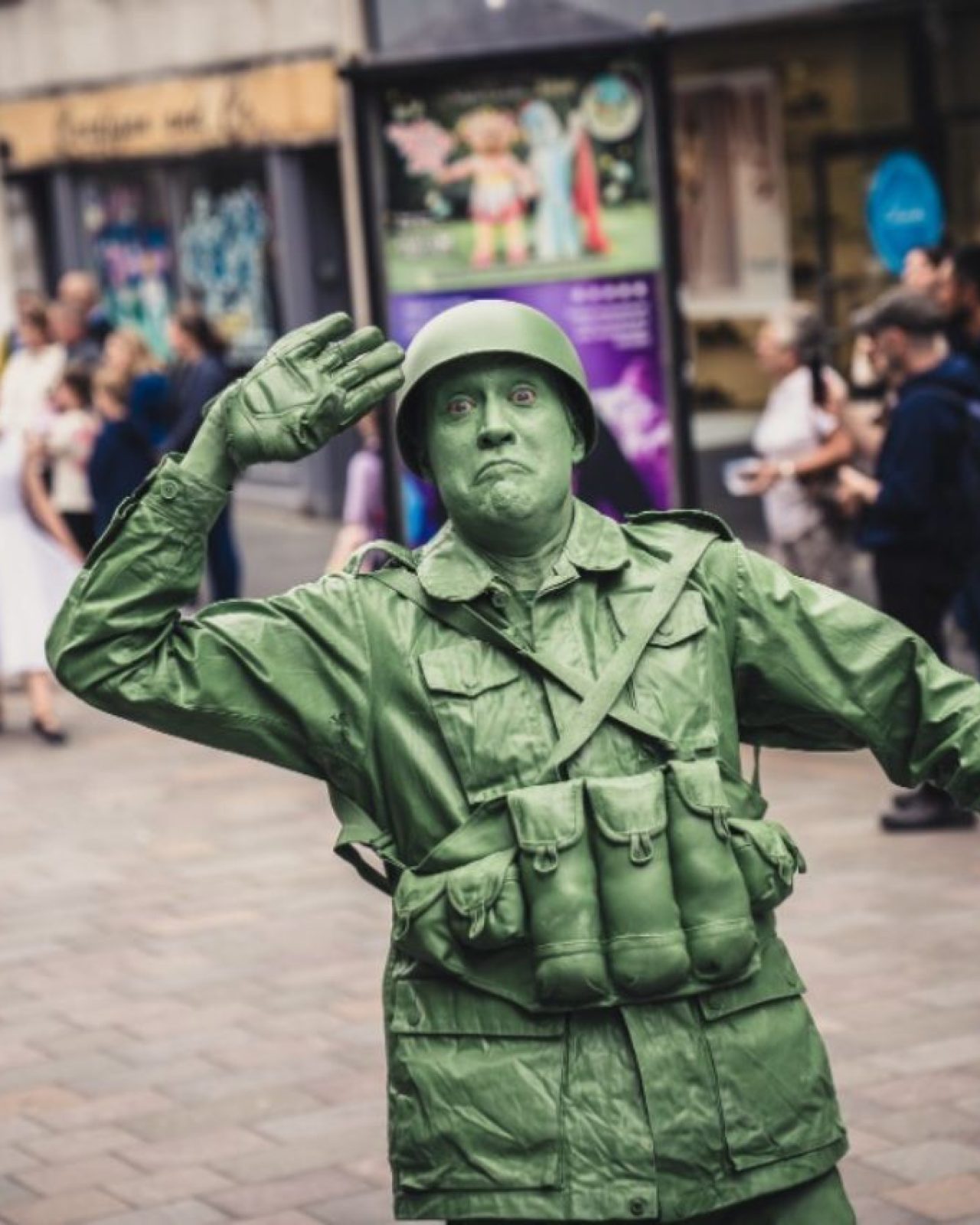 A man dressed as a green moving statue wearing a military uniform