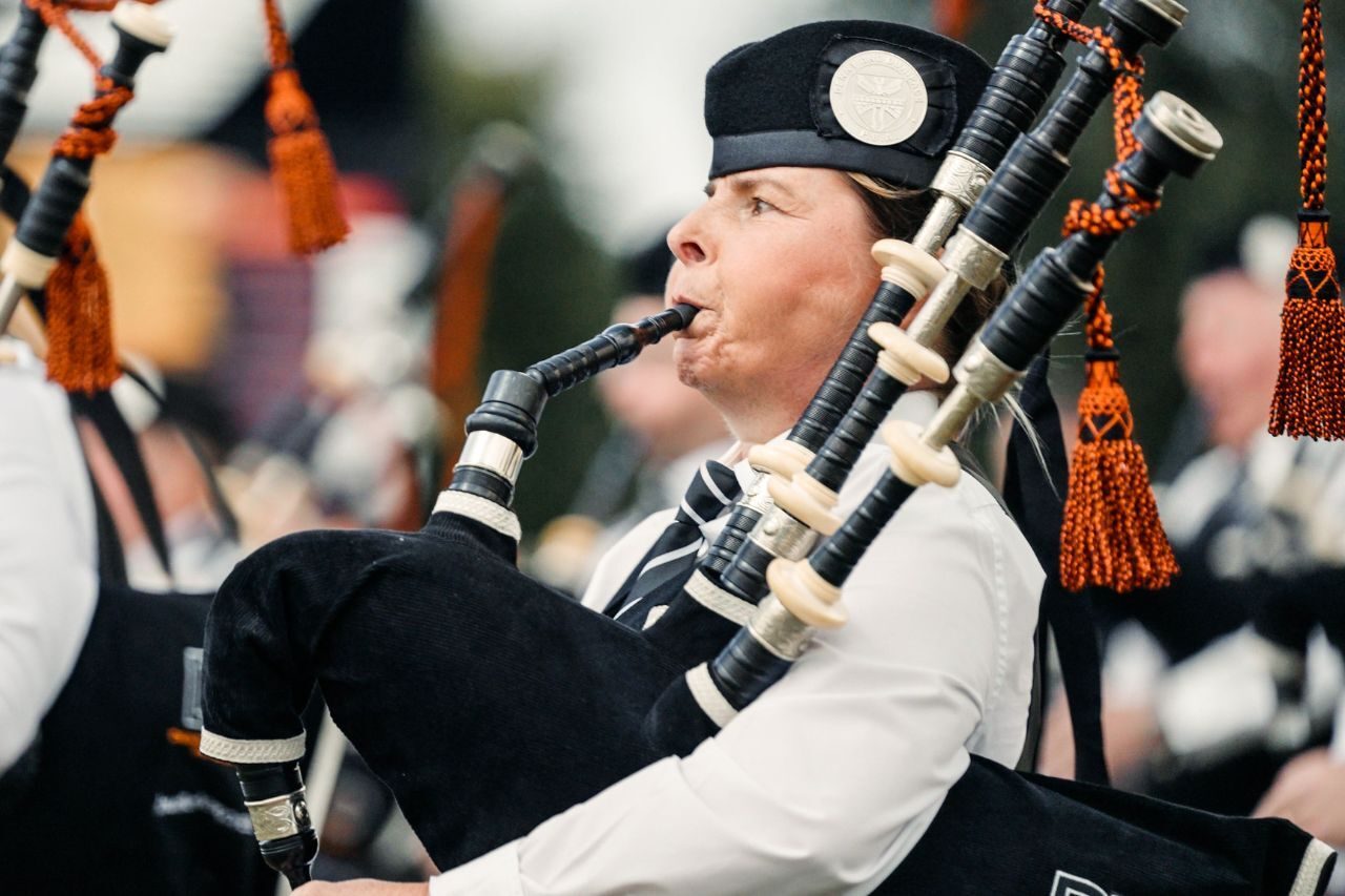 A woman in a white shirt playing black bagpipes with orange tassels.