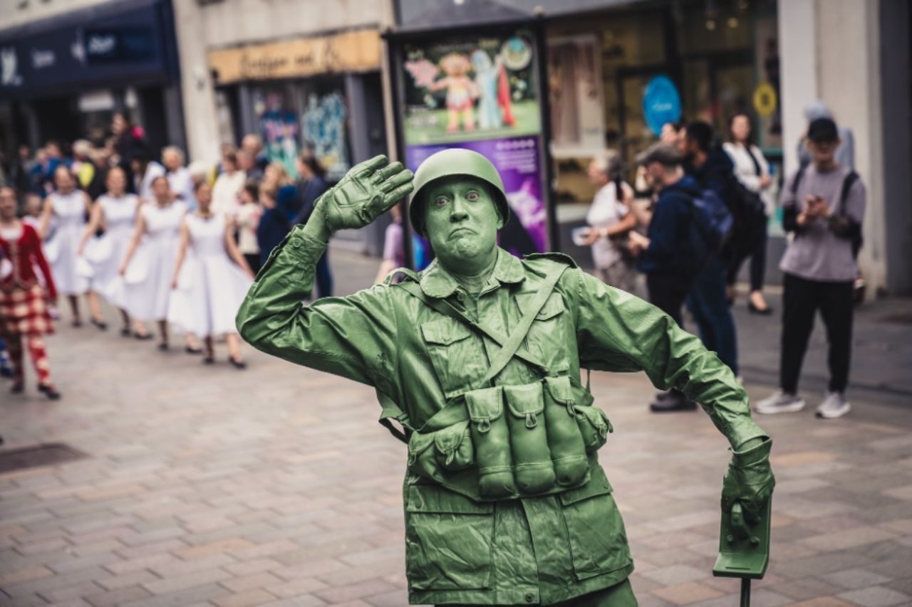 A man dressed as a green moving statue wearing a military uniform