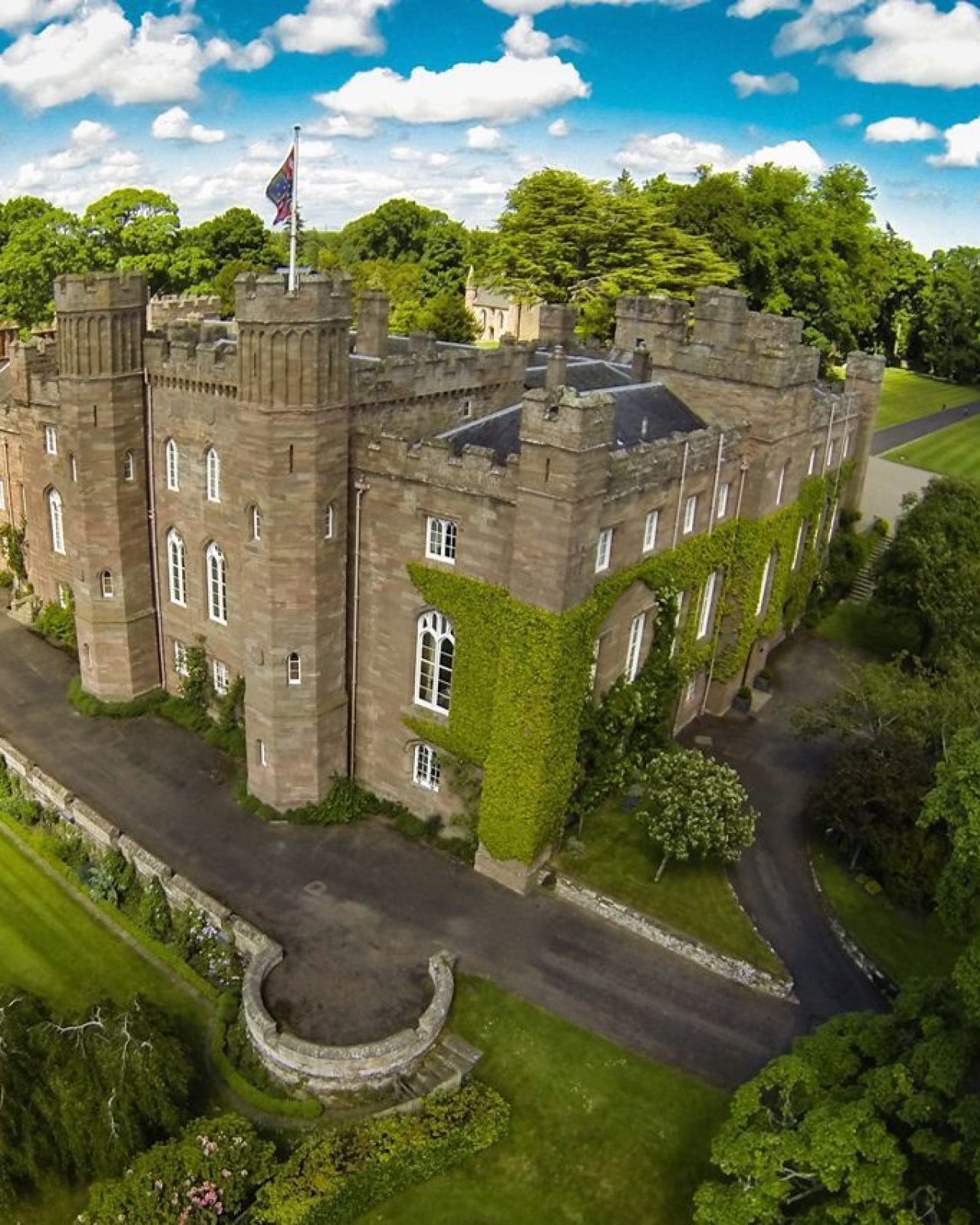 Large Scottish palace and its grounds with blue skies, green lawns and trees