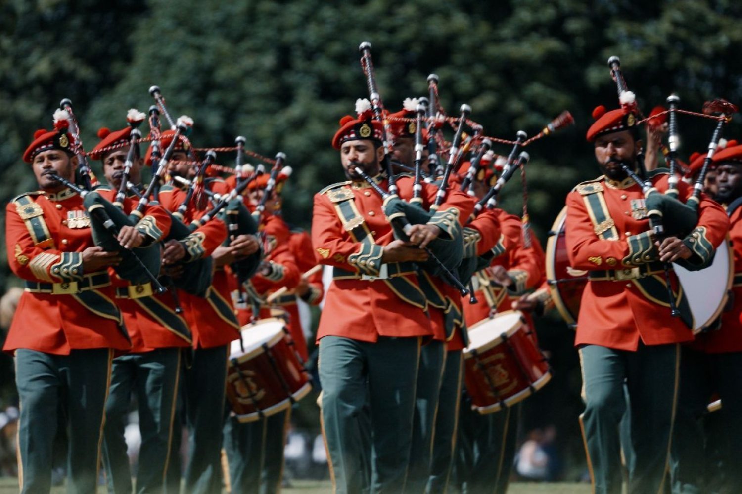 3 rows of men wearing red jackets playing the bagpipes